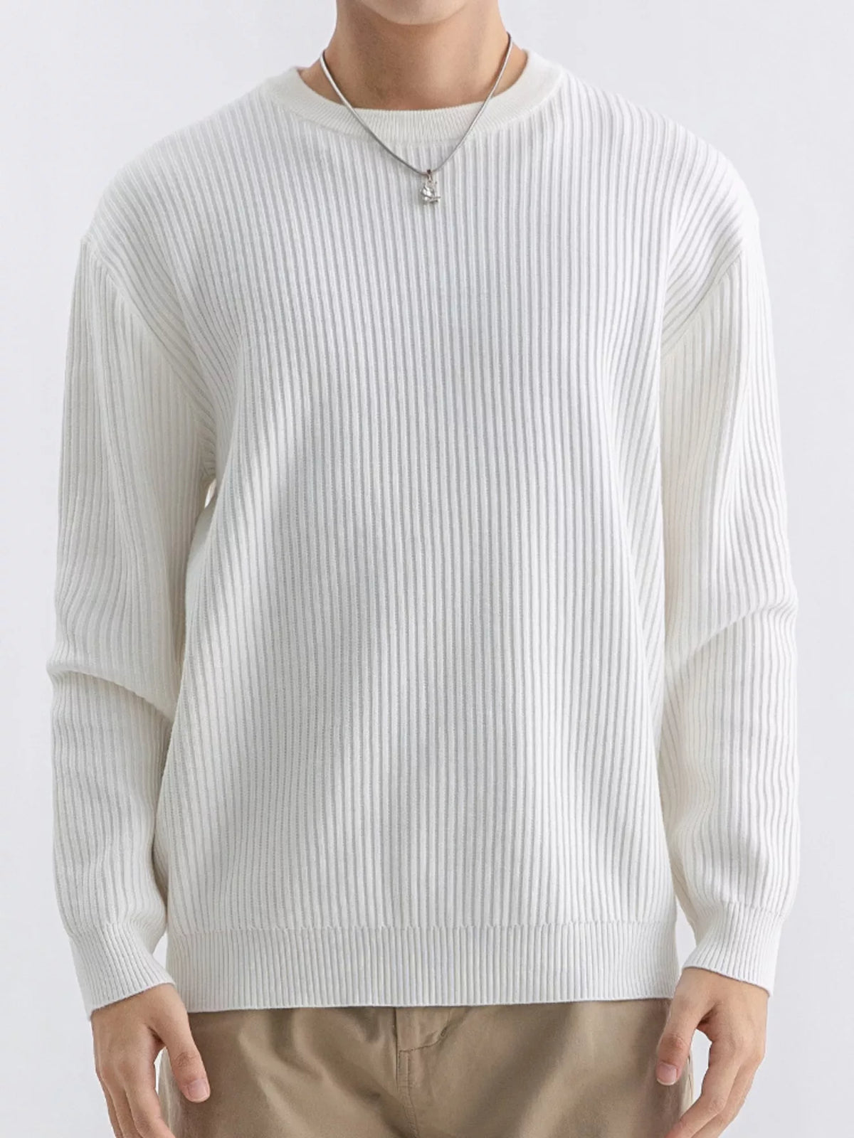 NEWYORKLISTED ATLAS MEN'S COLLECTION: A person wearing a ribbed long-sleeve crewneck sweater in off-white, paired with tan pants and a silver necklace, against a plain light background.