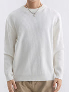 NEWYORKLISTED ATLAS MEN'S COLLECTION: A person wearing a ribbed long-sleeve crewneck sweater in off-white, paired with tan pants and a silver necklace, against a plain light background.