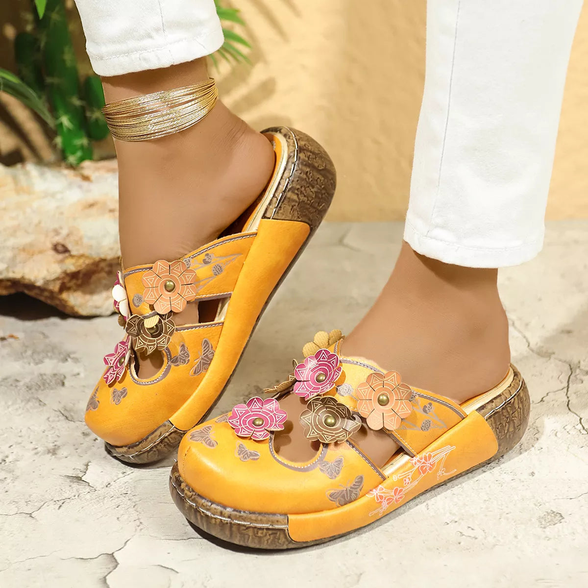 NEWYORKLISTED SHOE COLLECTION: Yellow sandals with floral designs worn by a person on a stone surface.