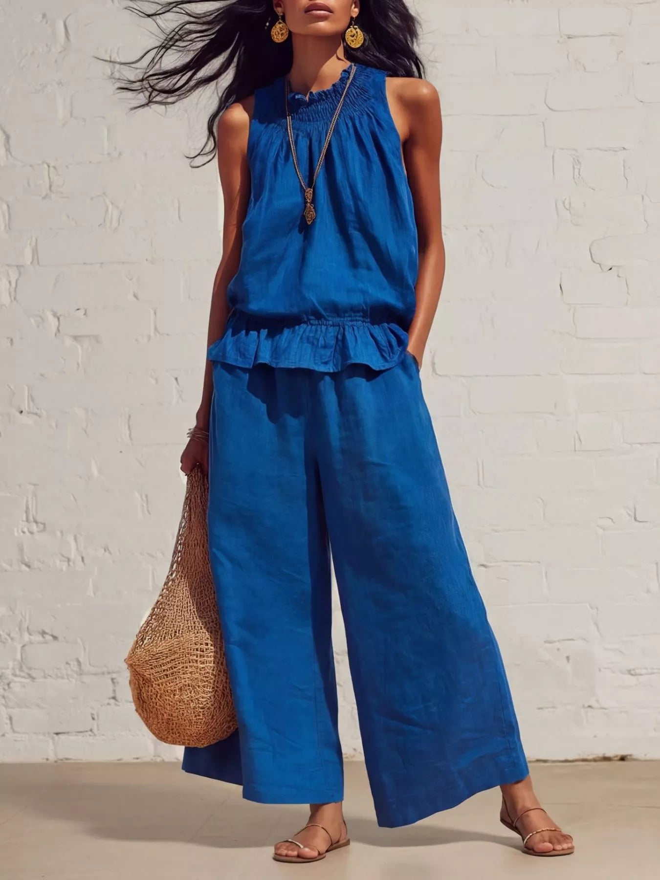 NEWYORKLISTED STYLE COLLECTION: Woman wearing a blue sleeveless top and wide-leg pants against a white brick wall.