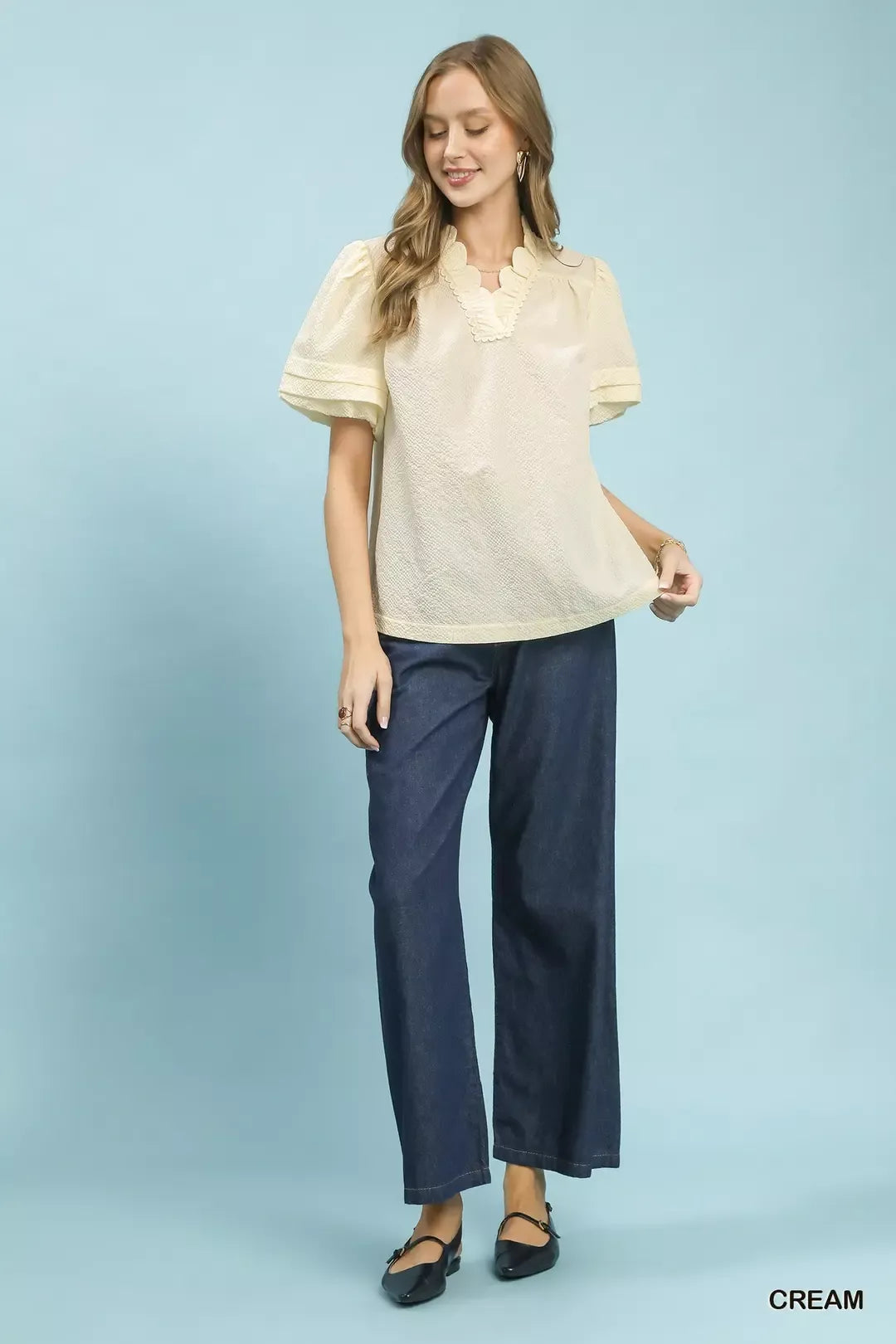 NEWYORKLISTED Style Collection: Woman wearing a cream blouse and navy pants on a light blue background