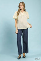 NEWYORKLISTED Style Collection: Woman wearing a cream blouse and navy pants on a light blue background