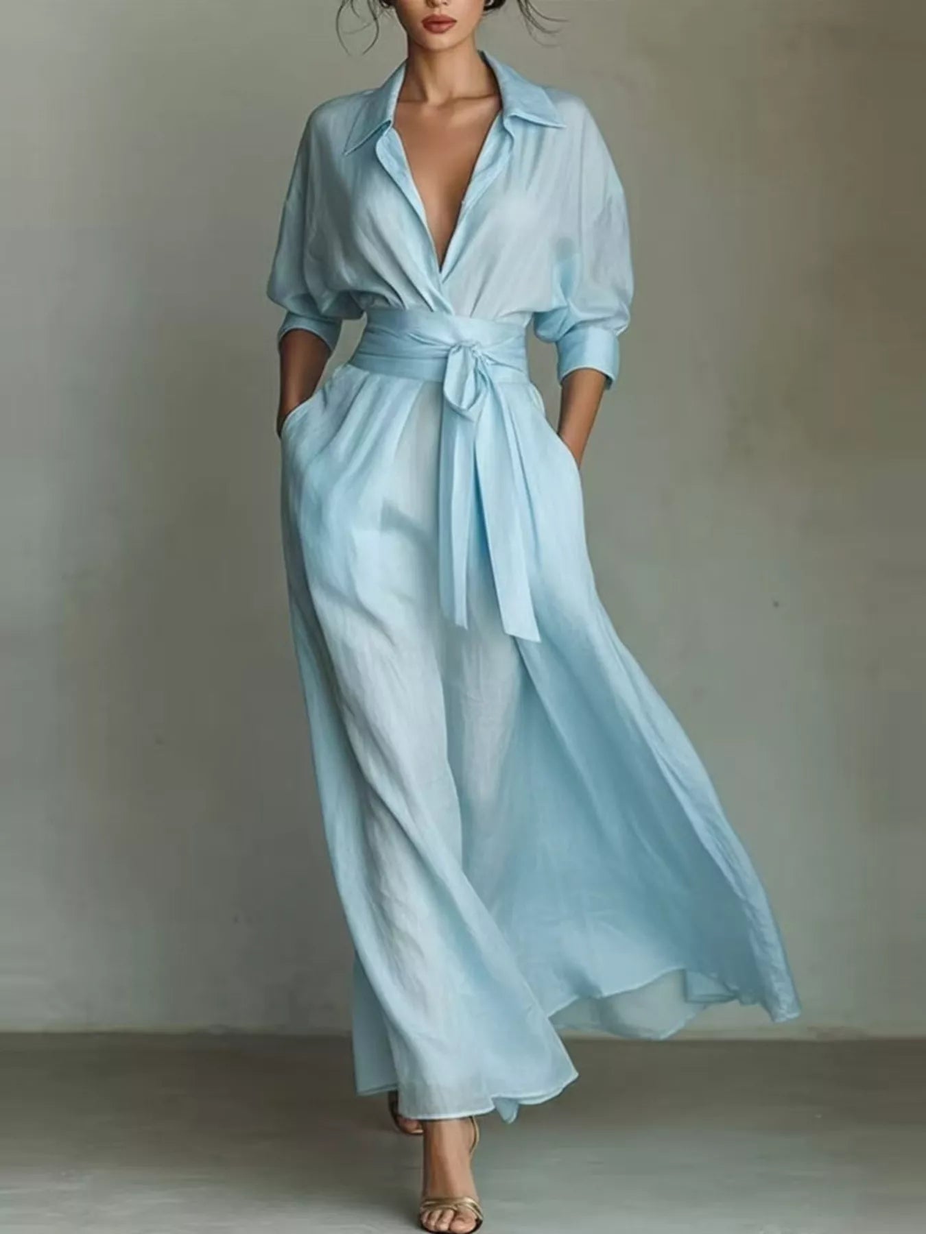 NEWYORKLISTED STYLE COLLECTION: A woman models a light blue wrap-style maxi dress with a tie waist, long sleeves rolled to the forearm, and side pockets, photographed against a neutral gray studio backdrop.