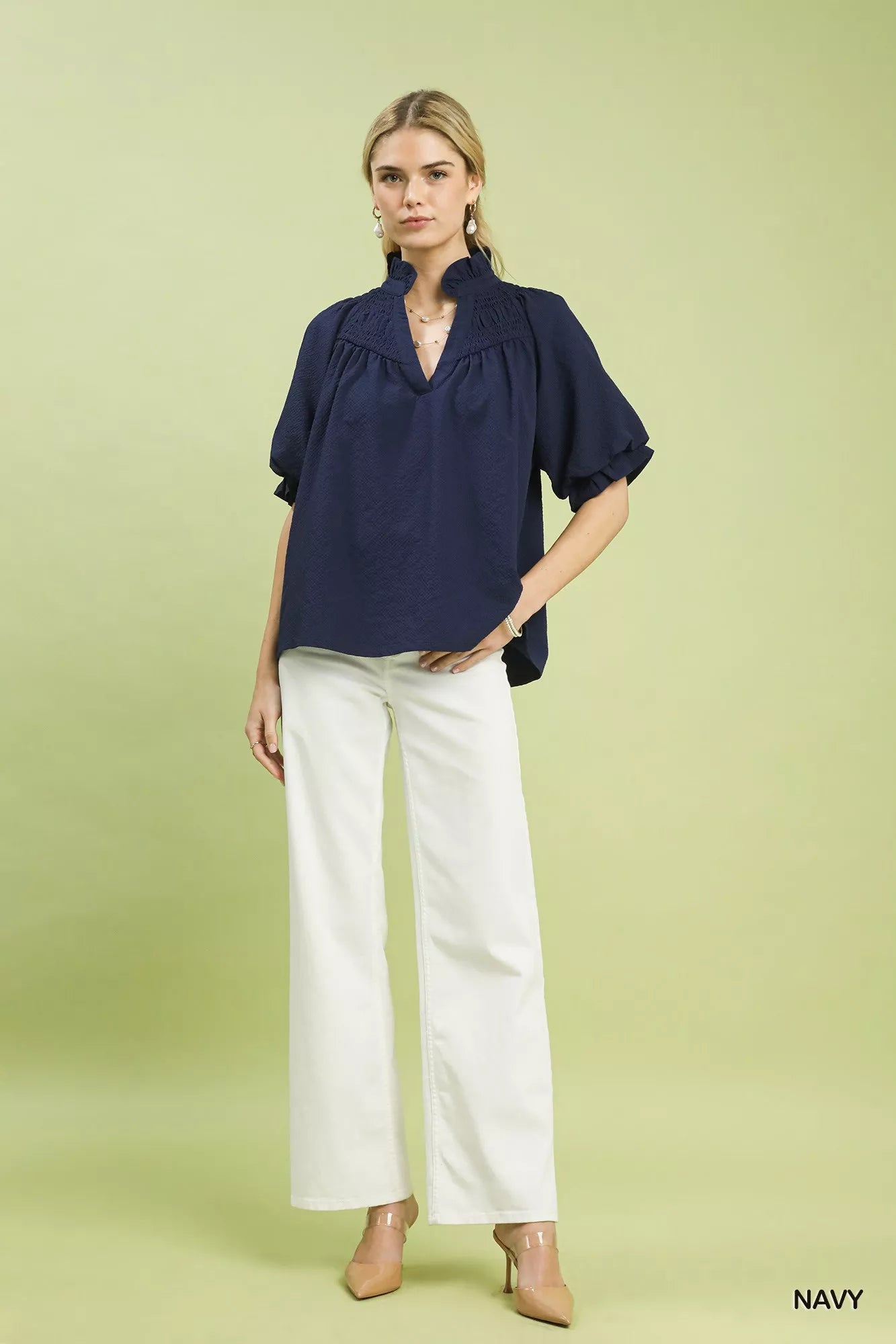 NEWYORKLISTED STYLE COLLECTION: Woman wearing a navy blouse and white pants on a light green background