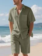 NEWYORKLISTED ATLAS MEN'S COLLECTION: Man wearing a green shirt and shorts on a beach with ocean and sky in the background