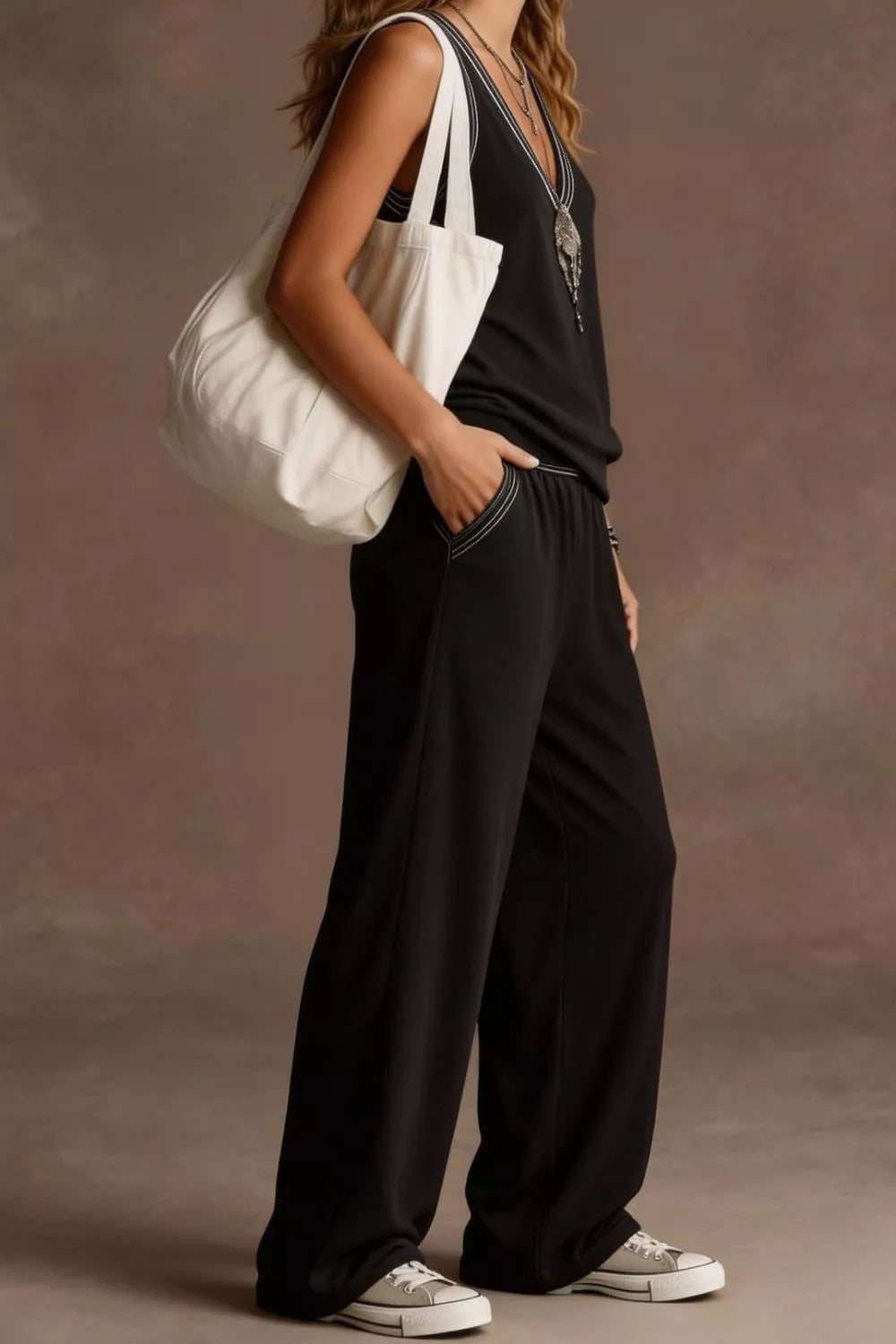 NEWYORKLISTED STYLE COLLECTION: Person wearing a black outfit with a white bag against a neutral background