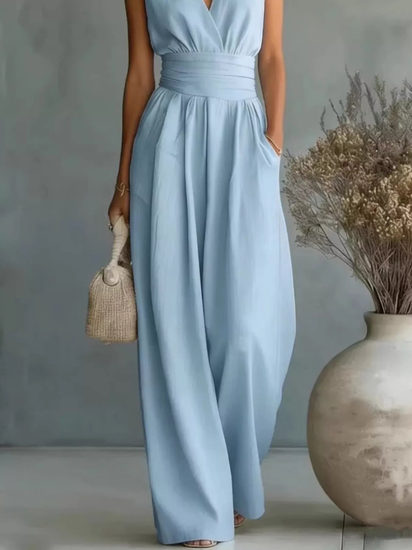 NEWYORKLISTED STYLE COLLECTION: Woman wearing a light blue dress holding a small bag, standing next to a vase with dried flowers.