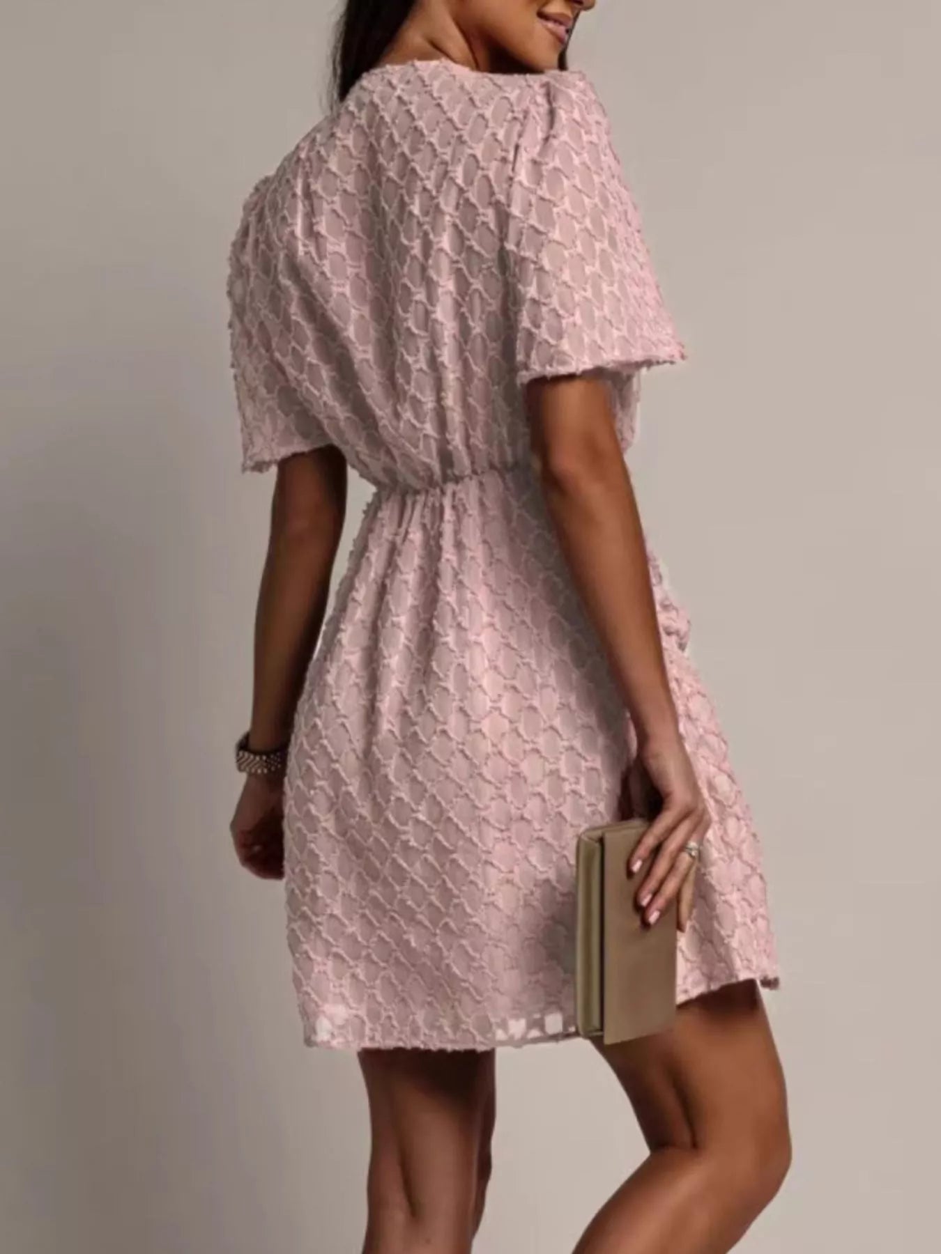 NEWYORKLISTED STYLE COLLECTION: Woman wearing a pink lace dress holding a book against a plain background