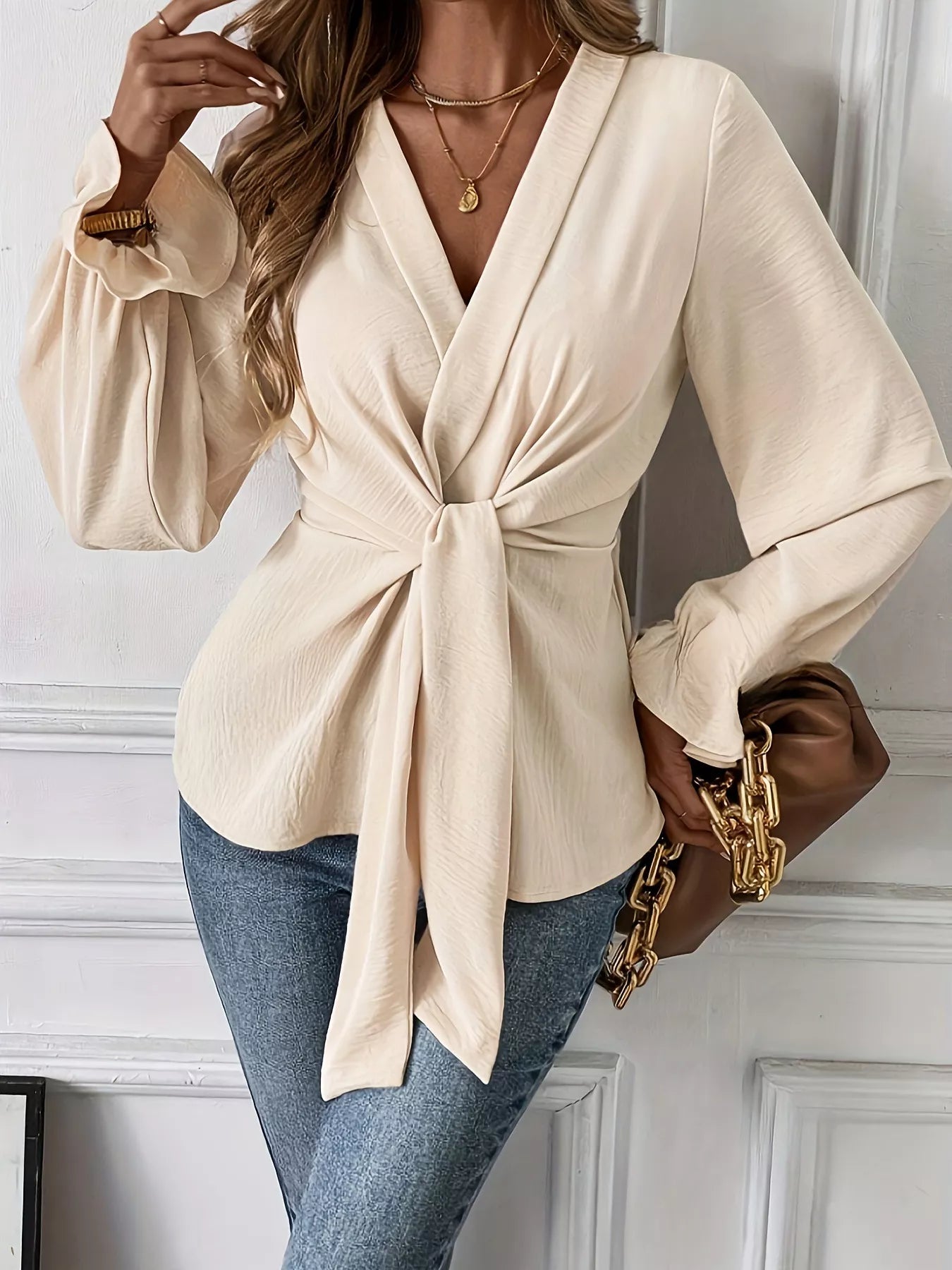 NEWYORKLISTED STYLE COLLECTION: Woman wearing a beige wrap top with blue jeans and a brown handbag.