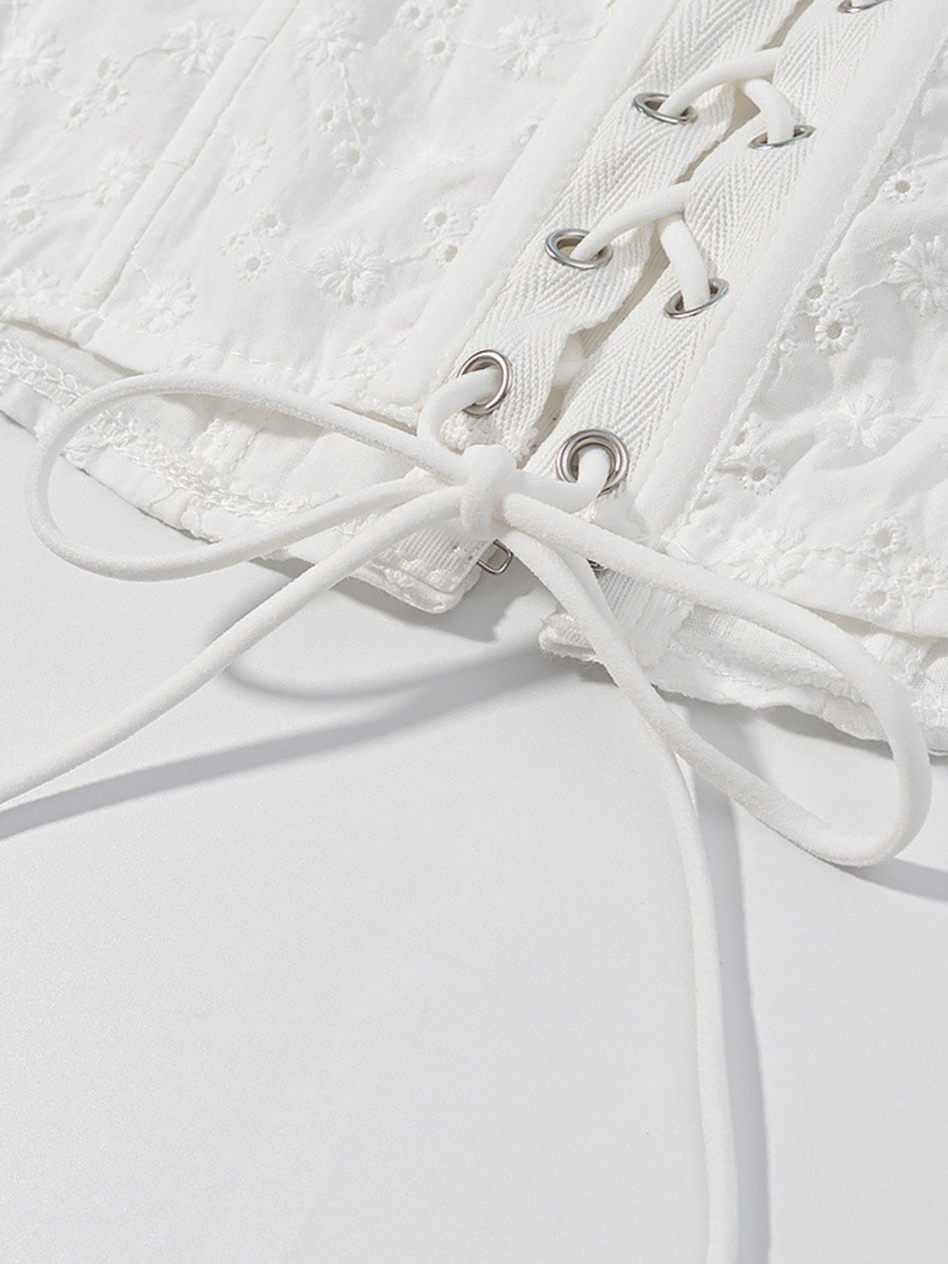 NEWYORKLISTED STYLE COLLECTION: Close-up of a white lace garment with laces on a light gray background