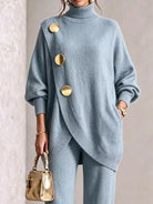NEWYORKLISTED STYLE COLLECTION:  A woman wearing a light blue knit turtleneck sweater with oversized gold buttons and matching knit pants, holding a small metallic gold handbag against a neutral indoor background.