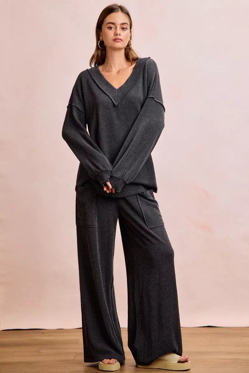 NEWYORKLISTED Comfort Collection: Woman wearing a dark gray outfit with wide-leg pants on a plain background