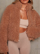 NEWYORKLISTED STYLE COLLECTION: Person wearing a fluffy tan jacket over a beige sports bra and leggings against a neutral background
