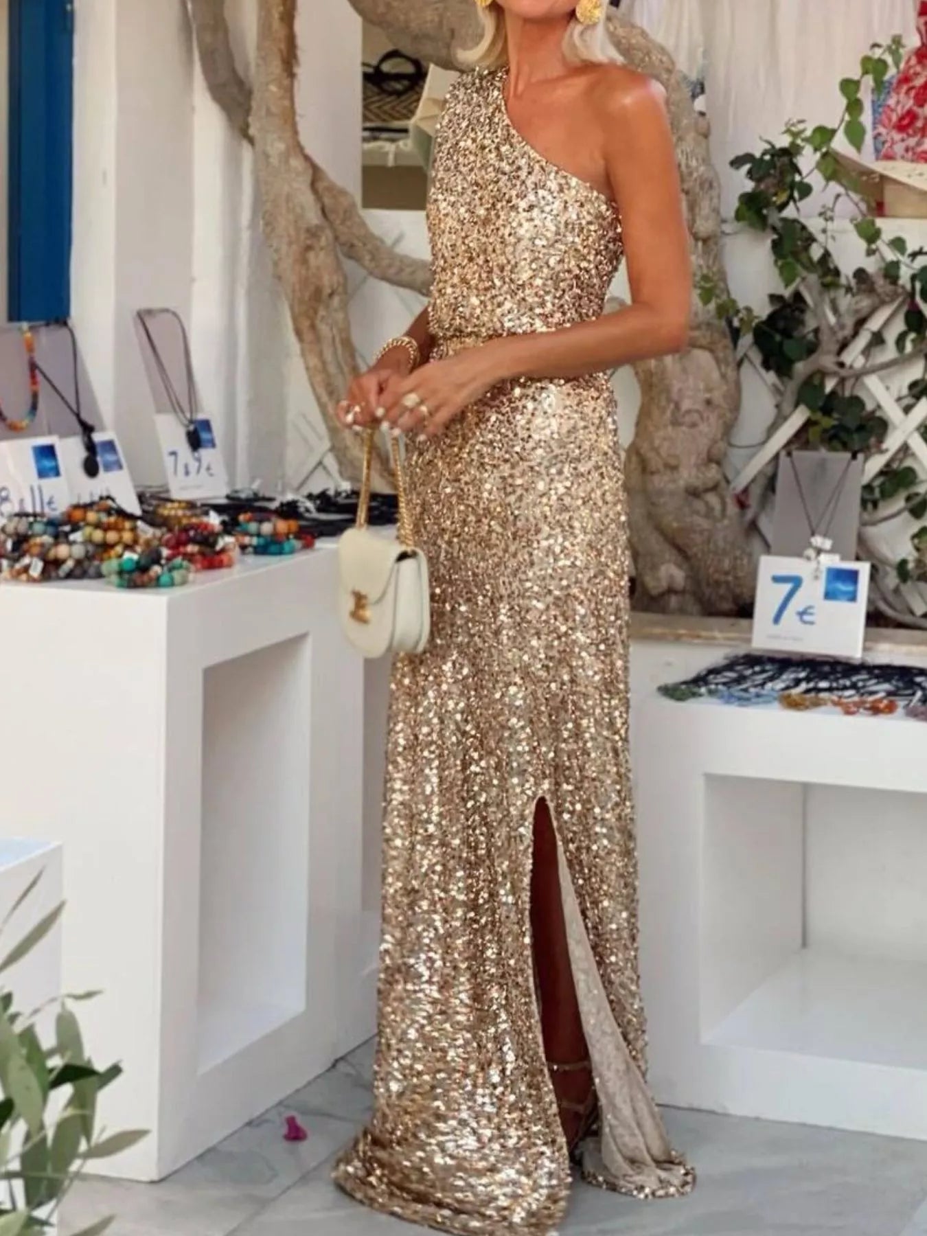 NEWYORKLISTED STYLE COLLECTION: Woman in a gold sequin dress standing in a store with jewelry displays.