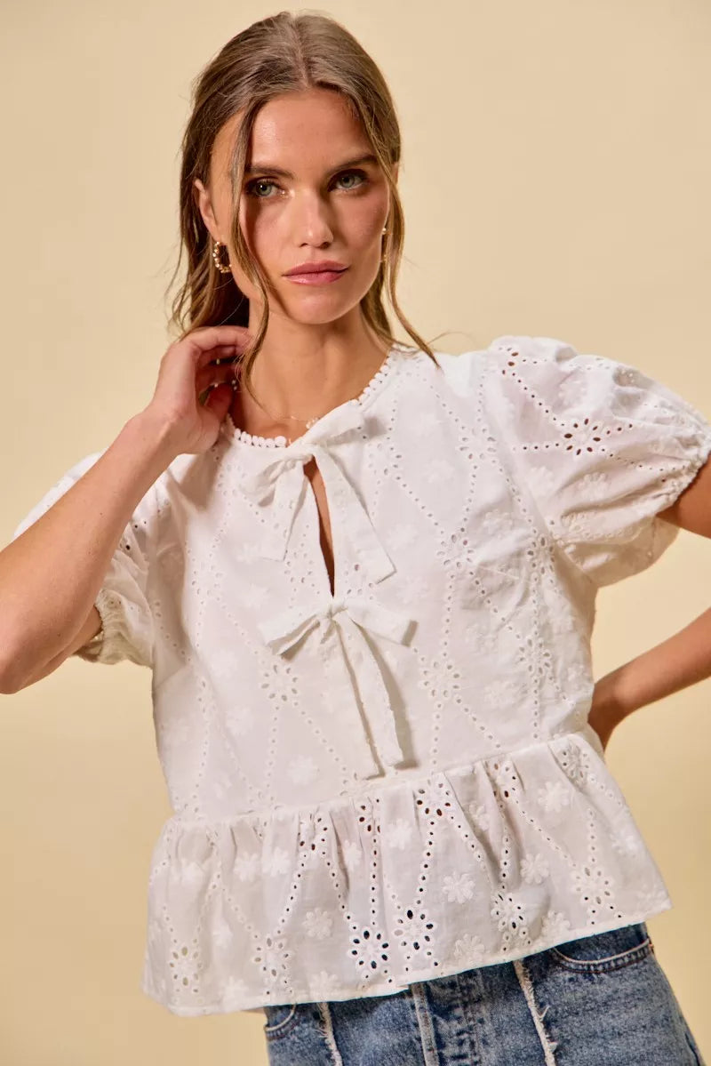 NEWYORKLISTED STYLE COLLECTION:  Woman wearing a white embroidered blouse with blue jeans on a beige background