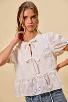 NEWYORKLISTED STYLE COLLECTION:  Woman wearing a white embroidered blouse with blue jeans on a beige background