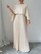 NEWYORKLISTED STYLE COLLECTION: Woman wearing a long, flowing beige dress with a draped top against a plain background