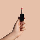 NEWYORKLISTED Cosmetic Collection: Hand holding a black lip gloss with red applicator against a beige background