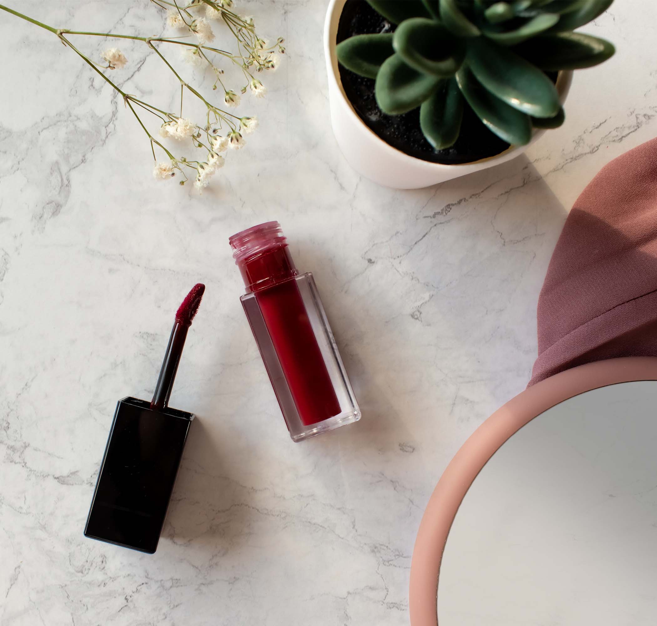 NEWYORKLISTED Cosmetic Collection: Red lip stain and applicator on a marble surface with a plant in the background