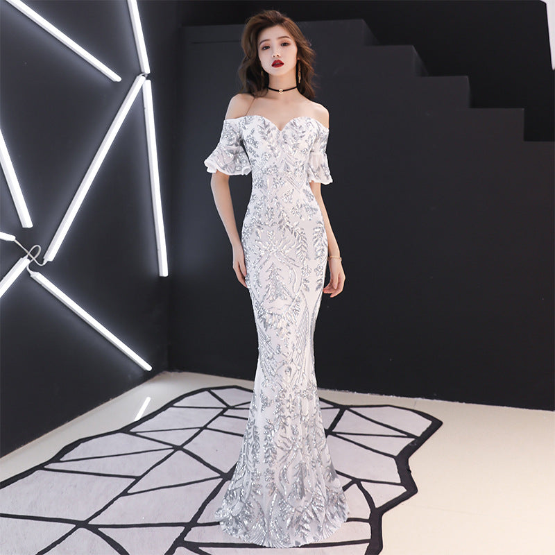 Woman in a white lace off-shoulder gown standing in a modern, geometrically lit room.