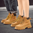 NEWYORKLISTED: Tan work boots with brand logo worn by a person on a dark surface