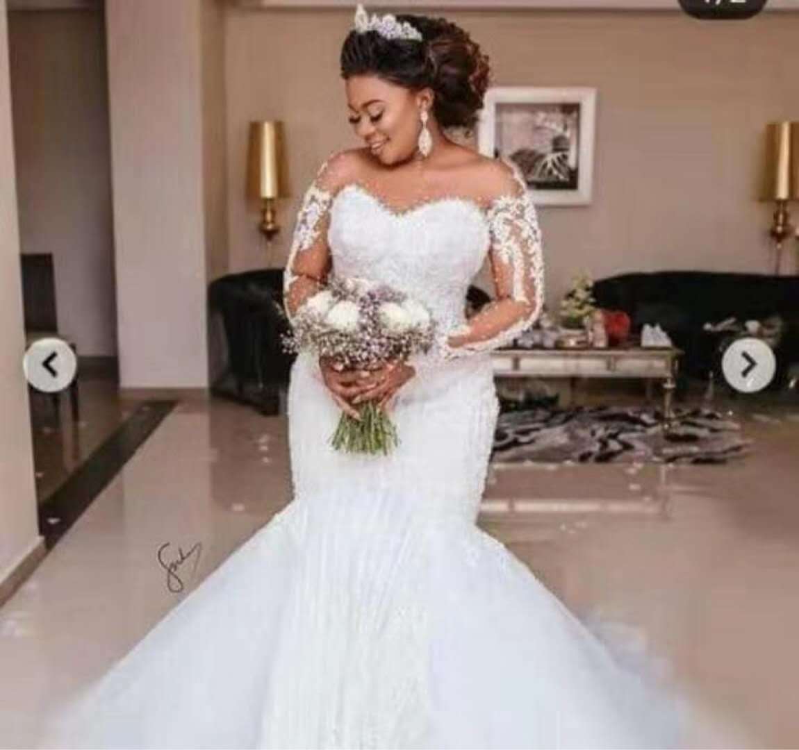 Woman in a white wedding dress holding flowers in a room.