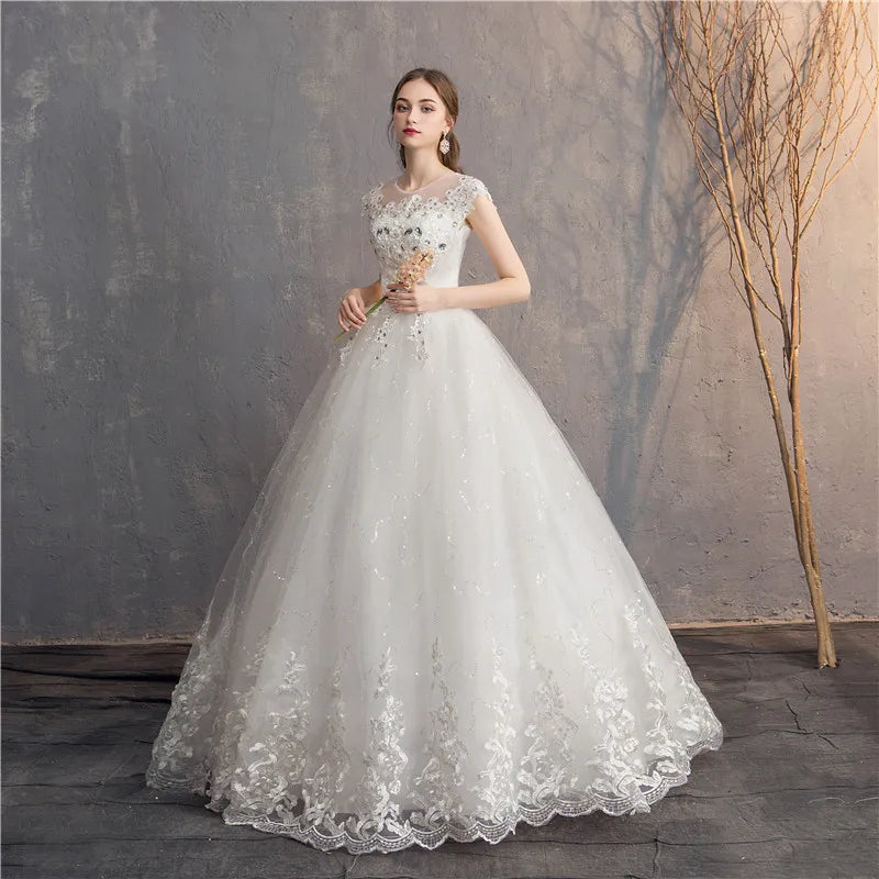 Woman in a white lace wedding dress holding flowers against a textured wall.