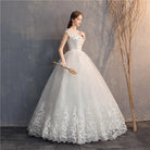 Woman in a white lace wedding dress holding a bouquet against a textured wall.