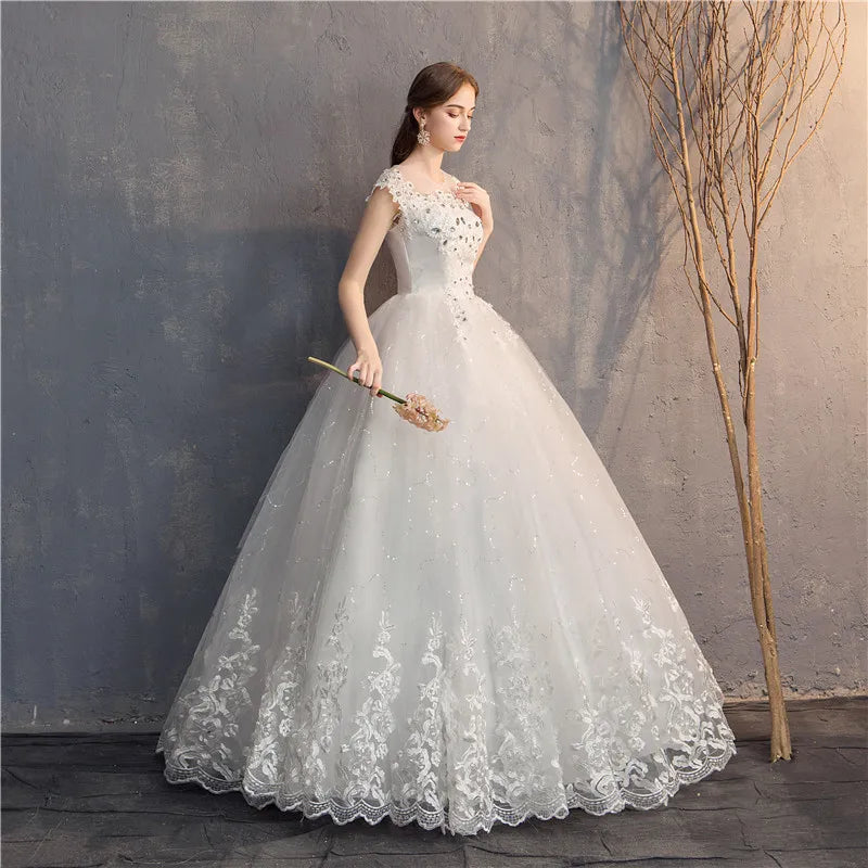 Woman in a white lace wedding dress holding a bouquet against a textured wall.