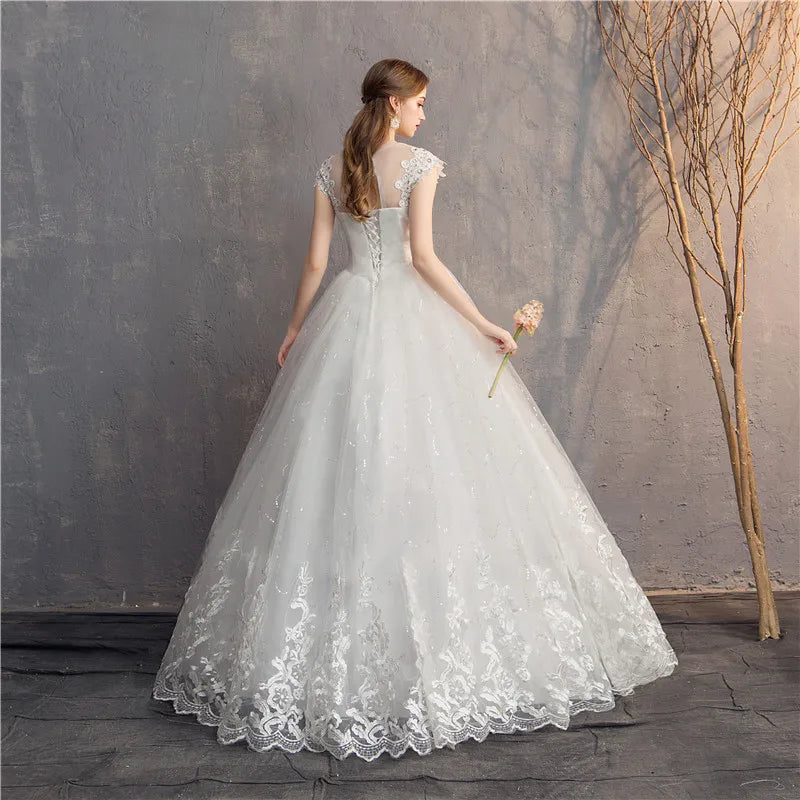 Woman in a white lace wedding dress holding a bouquet against a textured wall.