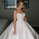 Woman wearing a white wedding dress with floral details, standing indoors.