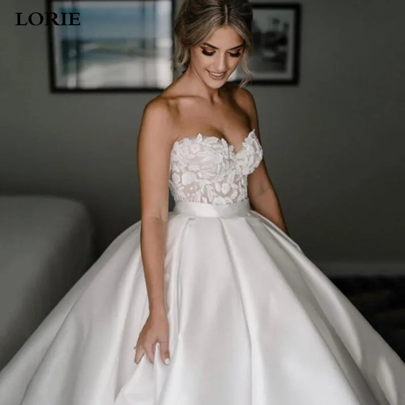 Woman wearing a white wedding dress with floral details, standing indoors.
