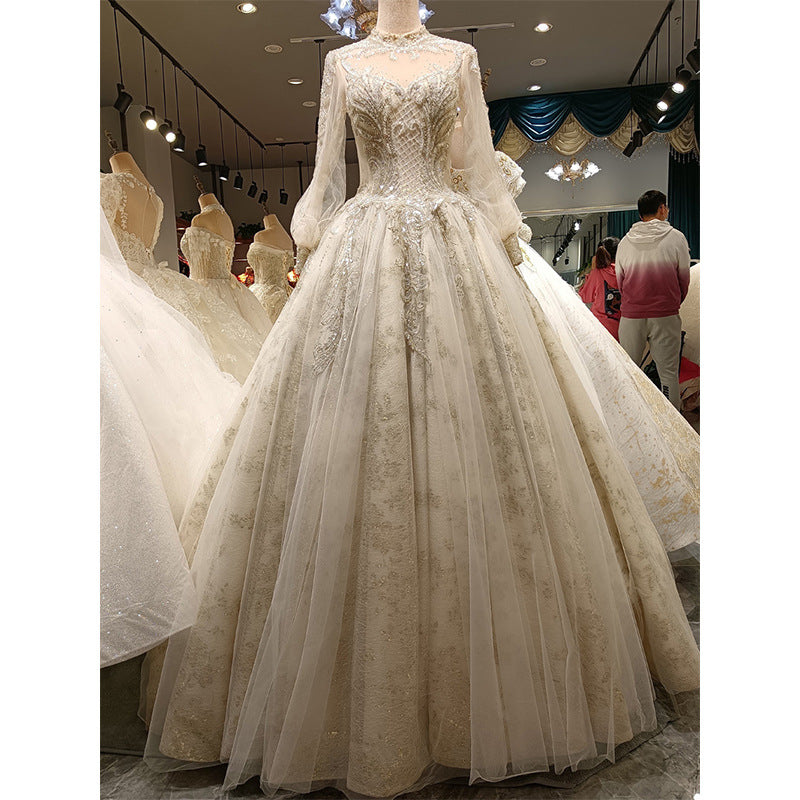Elegant white wedding dress on a mannequin in a store setting with other dresses and people in the background.