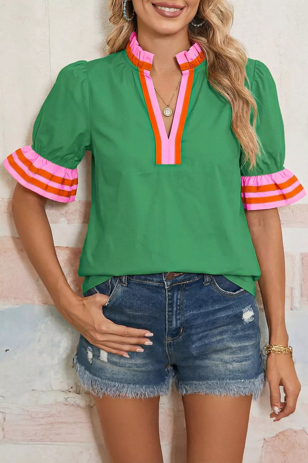 NEWYORKLISTED STYLE COLLECTION: Woman wearing a green blouse with colorful cuffs and denim shorts against a light background