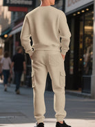 NEWYORKLISTED ATLAS MEN'S COLLECTION: A man viewed from behind wearing a cream-colored waffle-knit crewneck sweatshirt and matching cargo jogger pants on a city sidewalk.