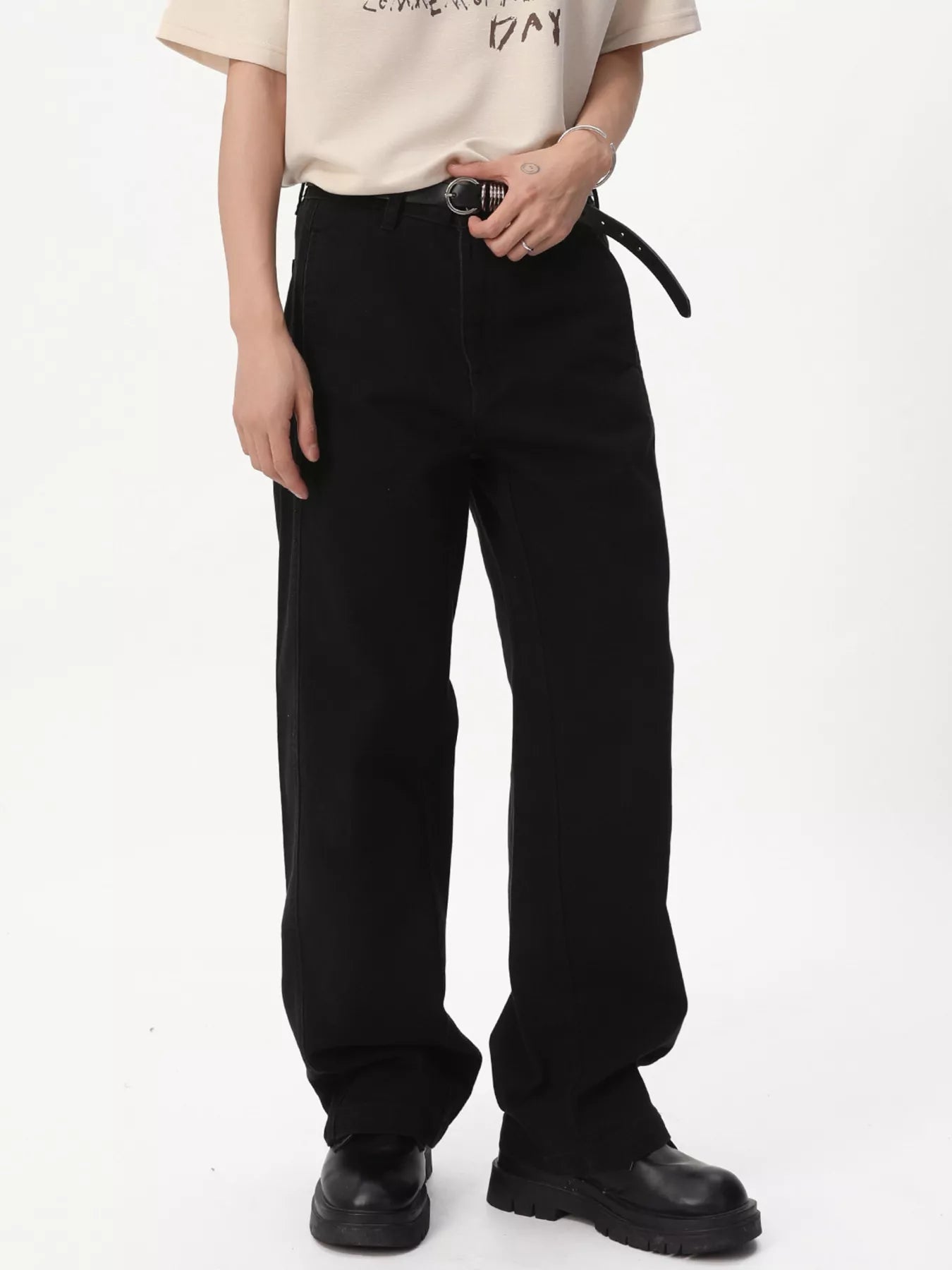 NEWYORKLISTED ATLAS MEN'S COLLECTION: A person wearing loose black wide-leg pants with a black belt, paired with a cream graphic T-shirt and black platform shoes, photographed against a plain white studio background.
