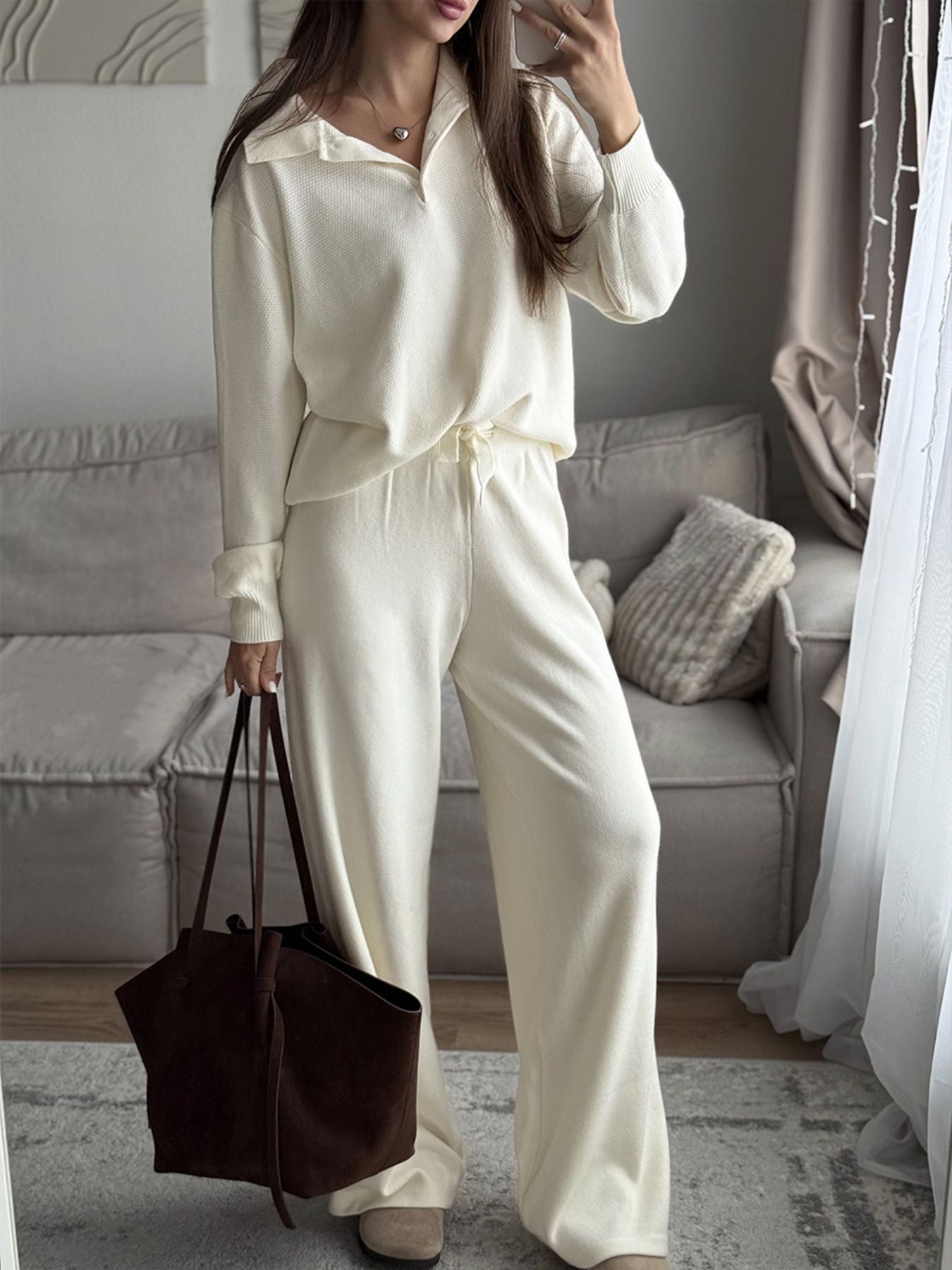 NEWYORKLISTED Comfort Collection: Woman in a white outfit holding a brown bag in a living room.