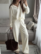 NEWYORKLISTED Comfort Collection: Woman in a white outfit holding a brown bag in a living room.