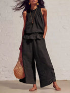NEWYORKLISTED STYLE COLLECTION: Woman wearing a black sleeveless top and wide-leg pants against a white brick wall.