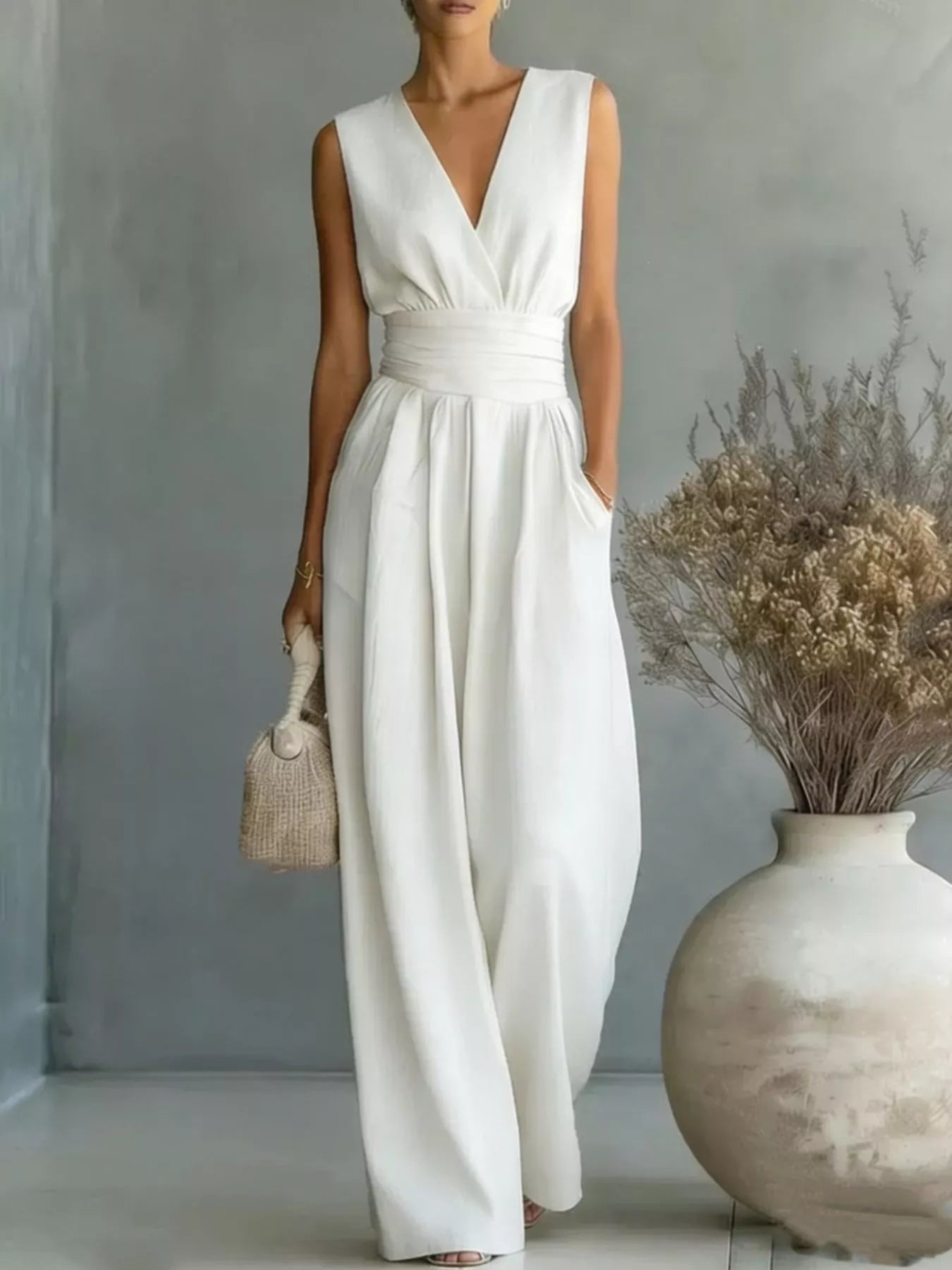 NEWYORKLISTED STYLE COLLECTION: Woman wearing a white sleeveless dress standing in a room with a vase and dried plants.