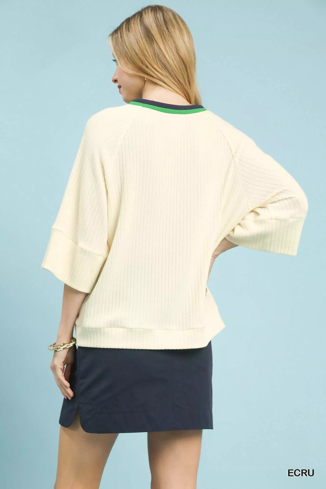 NEWYORKLISTED STYLE COLLECTION: Woman wearing a light-colored sweater and navy skirt on a light blue background