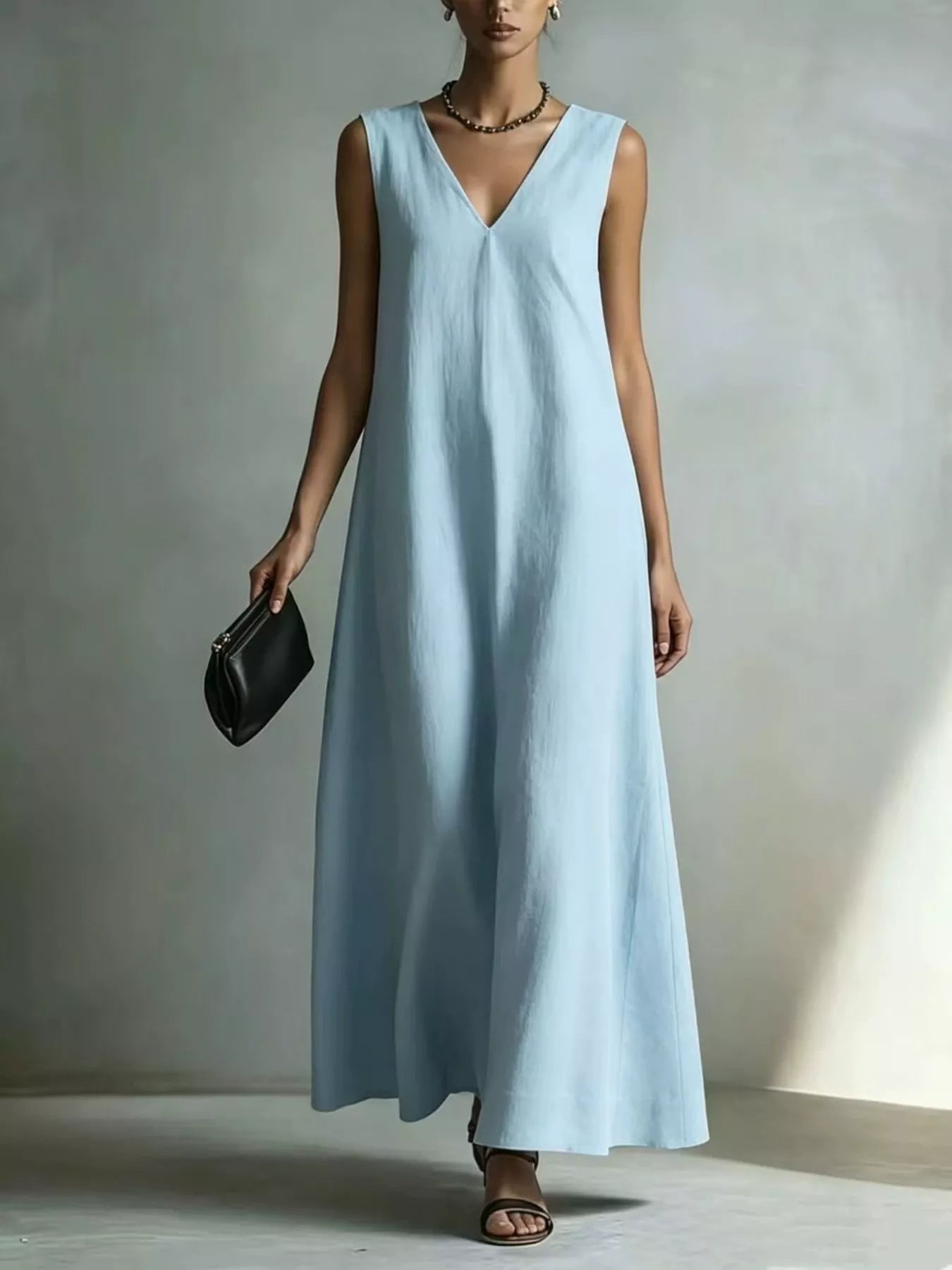 NEWYORKLISTED STYLE COLLECTION: A woman models a sleeveless light blue maxi dress with a V-neckline, holding a small black clutch bag against a neutral gray studio backdrop.