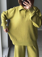 Person wearing a green sweater and pants taking a mirror selfie.