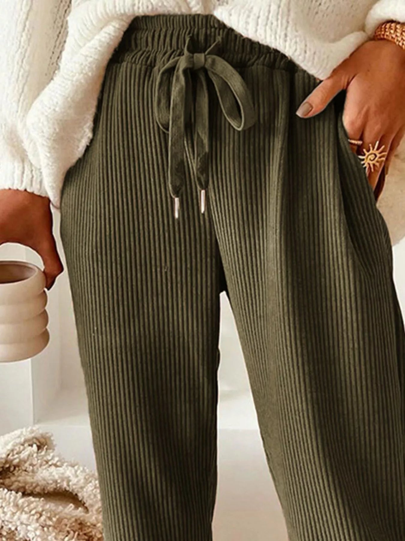 NEWYORKLISTED STYLE COLLECTION: Person wearing olive green ribbed pants with a white sweater and beige background