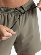 NEWYORKLISTED ATLAS MEN'S COLLECTION: Person adjusting a drawstring on olive green shorts against a white background