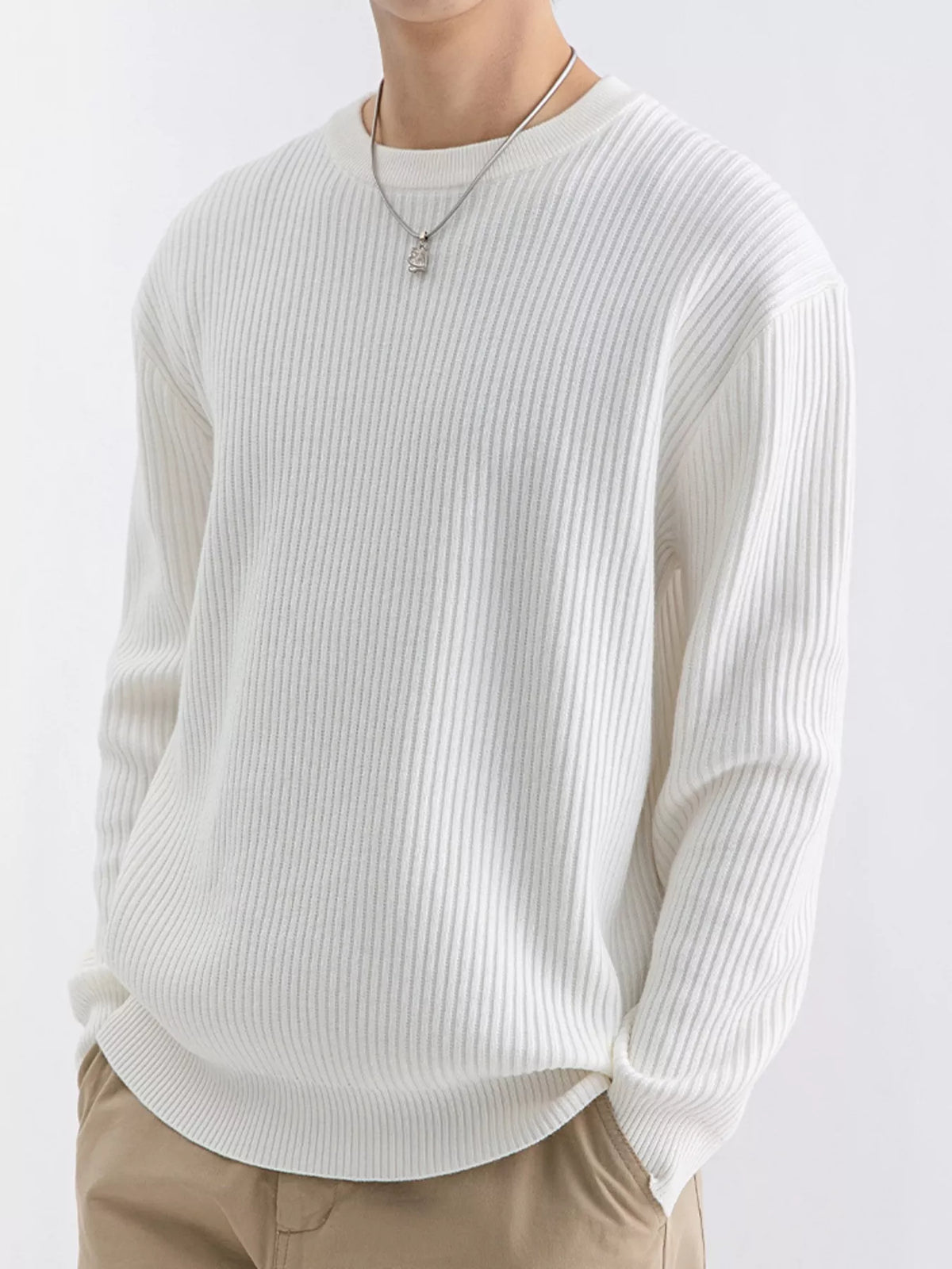 NEWYORKLISTED ATLAS MEN'S COLLECTION: A person wearing a ribbed long-sleeve crewneck sweater in off-white, paired with beige pants and a silver pendant necklace, against a plain light background.