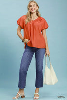 NEWYORKLISTED STYLE COLLECTION: Woman wearing an orange blouse and blue jeans holding a white bag on a light blue background