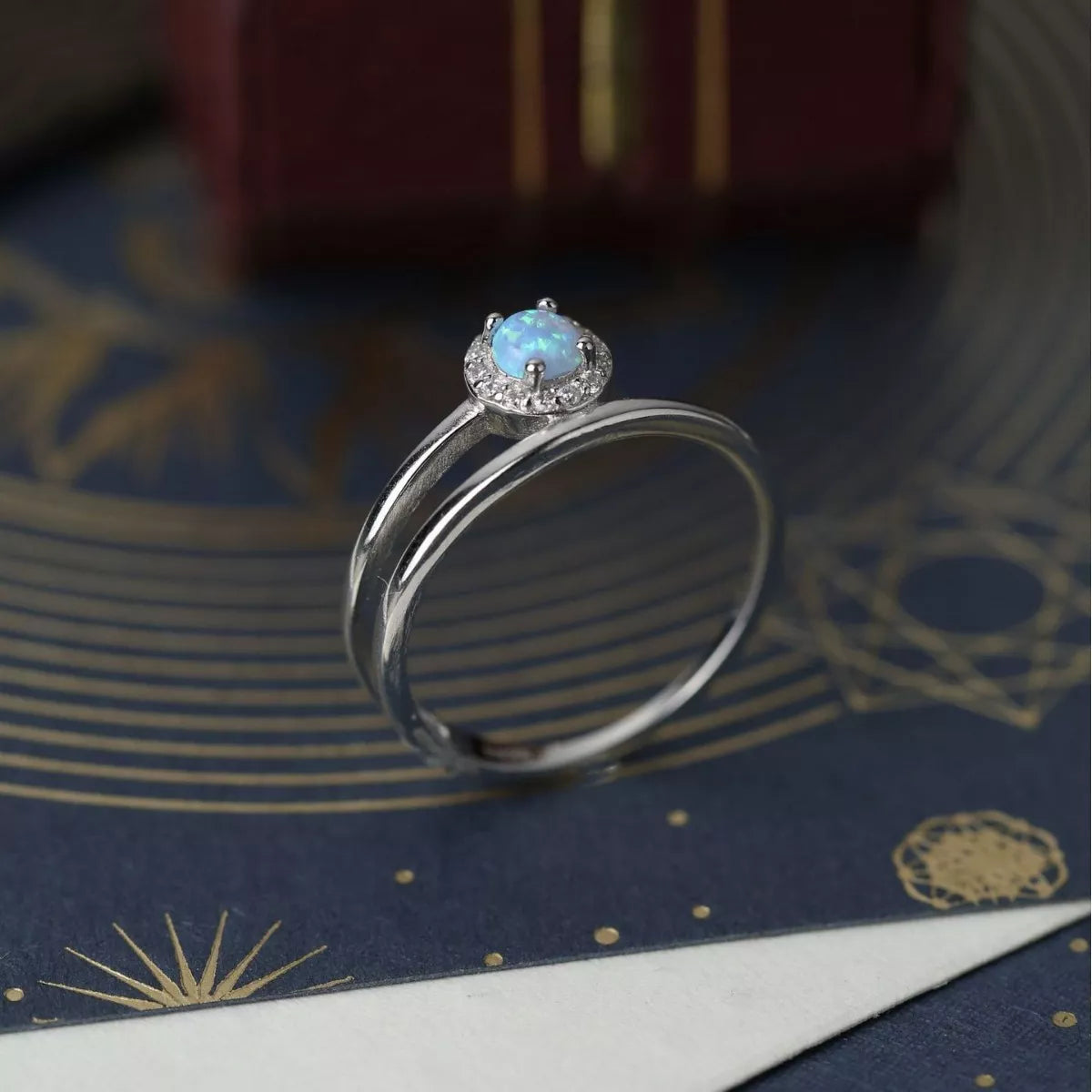 NYLD Glamour Collection by NEWYORKLISTED: Silver ring with a blue gemstone on a decorative surface
