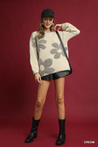 NEWYORKLISTED STYLE COLLECTION: Woman wearing a cream sweater with floral pattern, black shorts, and black boots on a red background