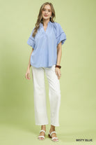 NEWYORKLISTED STYLE COLLECTION: Woman wearing a light blue blouse and white pants on a green background